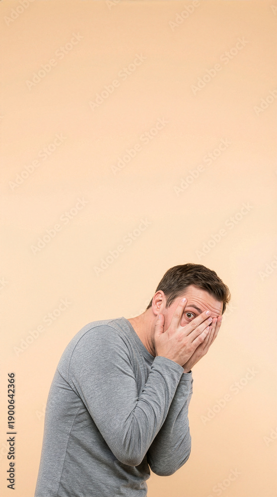Fototapeta premium Young Man Peeking Through Fingers With Fearful Expression