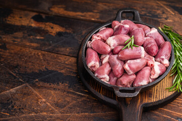 Fresh poultry hearts in black skillet, enhanced by aromatic rosemary and garlic cloves — rustic food photography.
