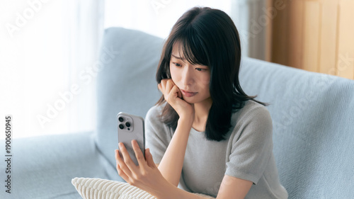 Quadro su tela スマートフォンを見ながら考え込む女性,自宅のソファで過ごす時間, A Woman Looking Thoughtful While Checking Her S