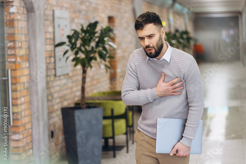 Young man experiencing chest pain an emergency health condition, suffering discomfort in the work or office environment