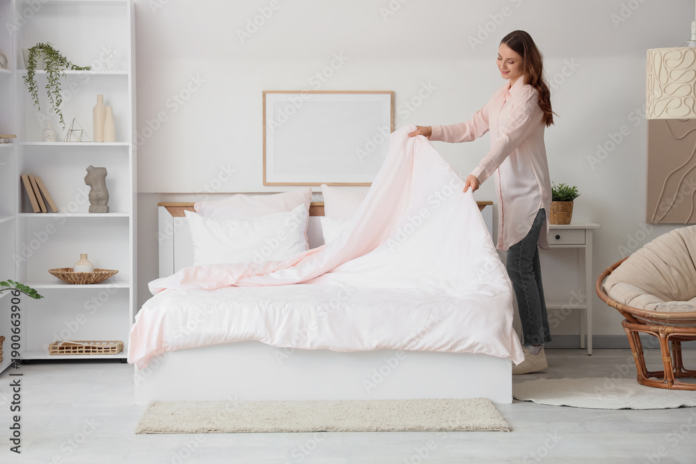 Fototapeta premium Young happy woman making bed with pink blanket at home