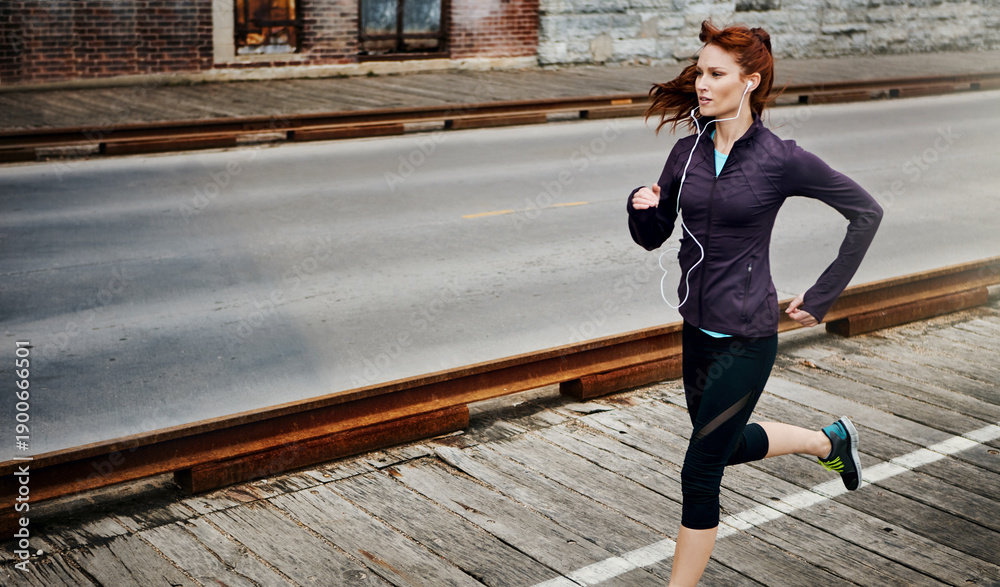 Fototapeta premium Fitness, woman and running with earphones in city for speed training, exercise playlist or cardio. Space, runner and music outdoor for jogging routine, health challenge and streaming workout podcast