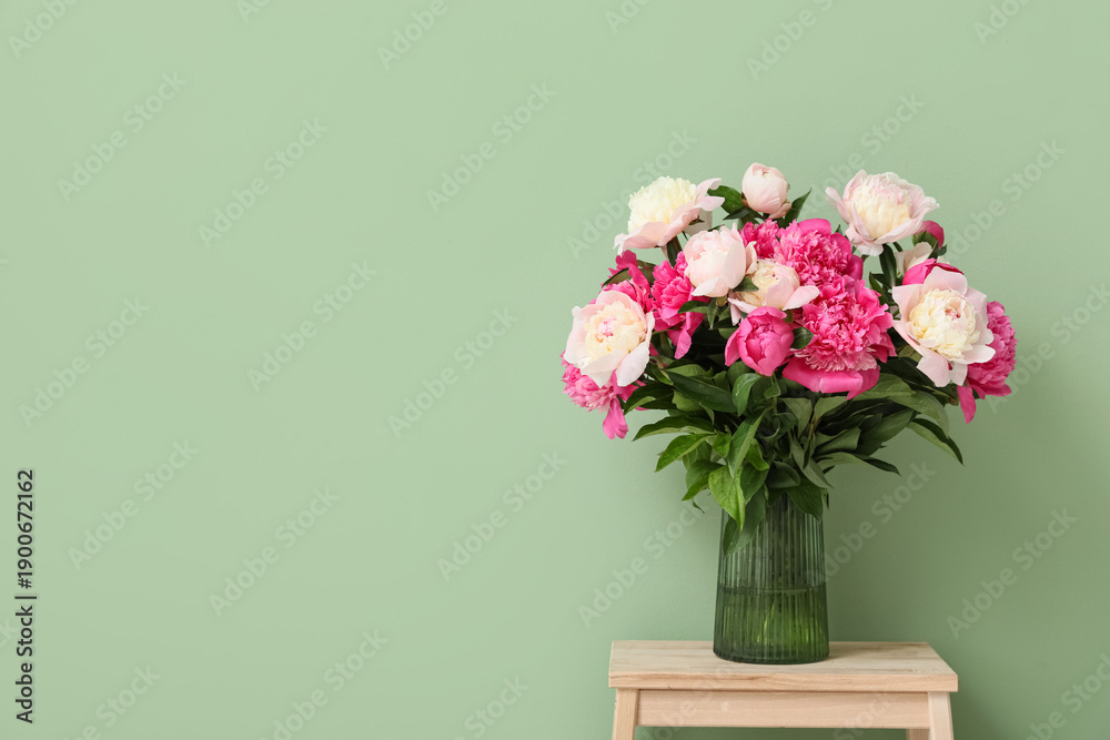 Fototapeta premium Vase with beautiful peony flowers on stool near green wall in room, closeup