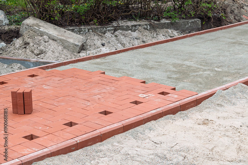 фотографія Red paving bricks form new sidewalk section on compacted base, with alignment gaps for drainage and expansion joints in courtyard