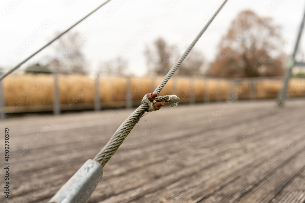 Fototapeta premium Steel wire rope connection detail on a weathered wooden deck with blurred background of dry reeds and bare trees in autumn