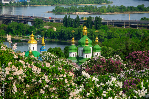 Foto Vydubychi Monastery with green and golden domes framed by blooming lilacs, overl