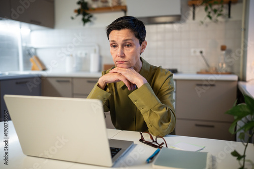 Obraz na plátne Thoughtful upset senior businesswoman works on laptop from home, looking at screen with lost exhausted expression, tiredness at work