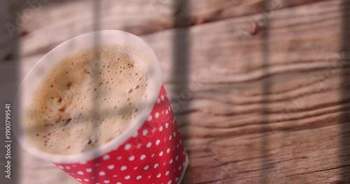 Fototapeta Sitting red polkadot cup on wood table with frothy coffee, shadow lines and sunlight, copy space