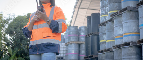 Canvastavla A person wearing a bright safety jacket and jeans stands near stacked barrels in a storage area
