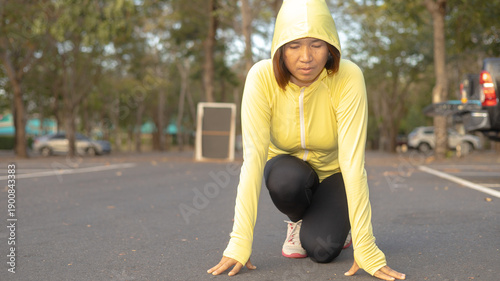 Bild auf Leinwand A woman in a yellow hoodie is kneeling down in a parking lot, getting ready to run