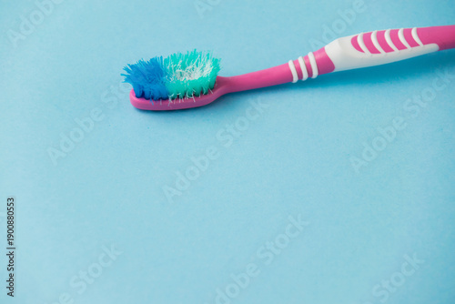 Old pink toothbrush on a paper blue background. Concept of proper oral care and timely replacement of toothbrushes