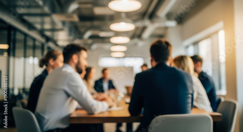 Blurred business professionals engaged in a collaborative meeting around a conference table in a modern office setting with blurred background and overhead lighting