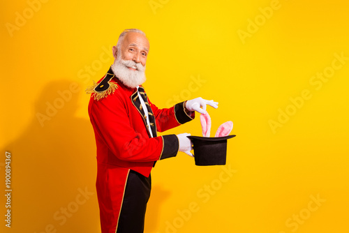 Εκτύπωση καμβά Elderly magician in red circus costume performs bunny trick against bright yello