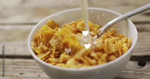 Fototapeta White ceramic bowl of corn flakes receiving milk pouring on rustic tabletop, spoon and heart bokeh