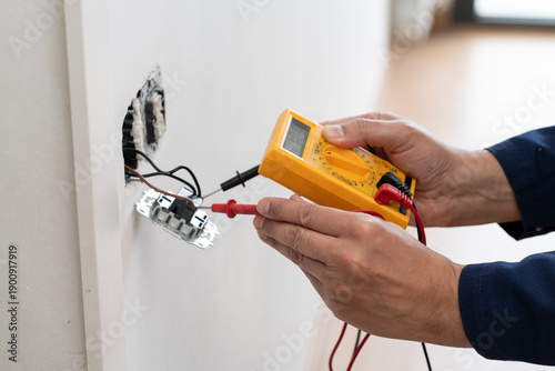 Close-up on an hands of electrician fixing an electrical outlet and measuring the voltage at a house - home improvement concepts