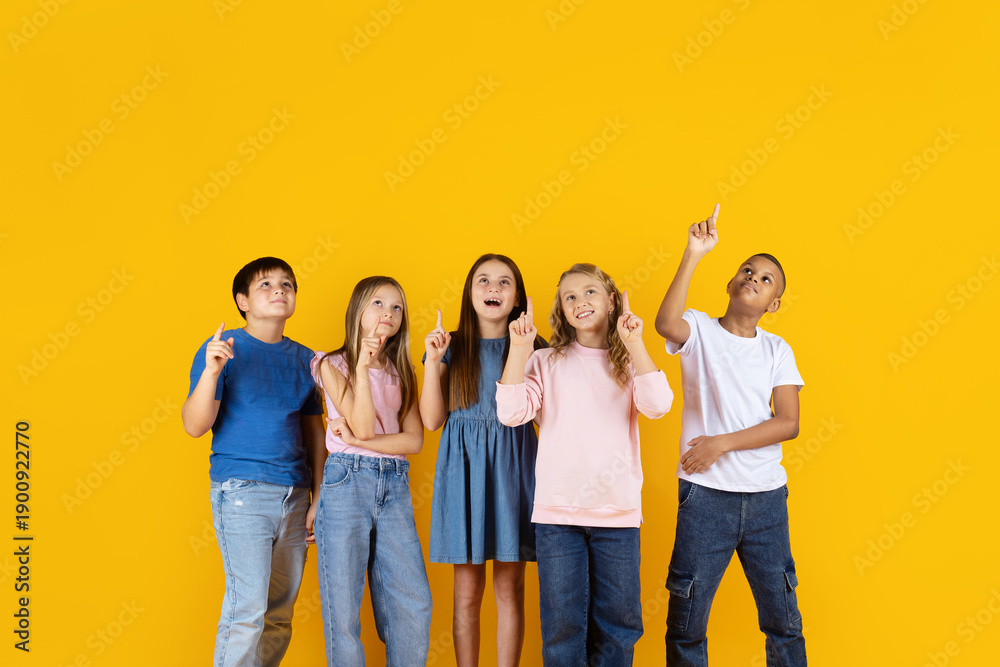 Fototapeta premium Preteen children looking up and pointing on yellow background, expressing curiosity and imagination. Education, creativity, learning, and future thinking concept