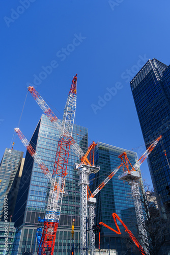 Modern construction cranes against a bright blue sky in a business district.