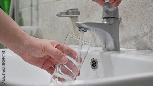 Close up of filling glass with water from sink faucet in bathroom