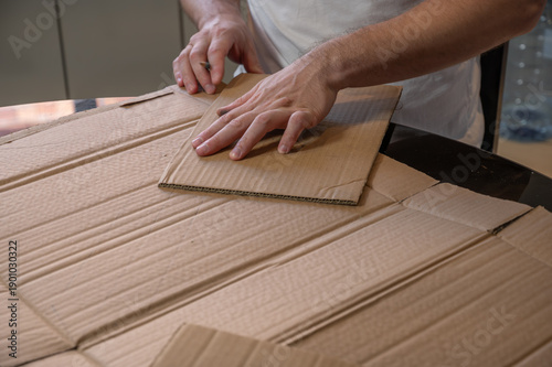 Close-up of hands working on a cardboard prototype at a desk. Startup project concept, product development, prototyping process, creativity, and innovation. Hands-on work, no face visible.