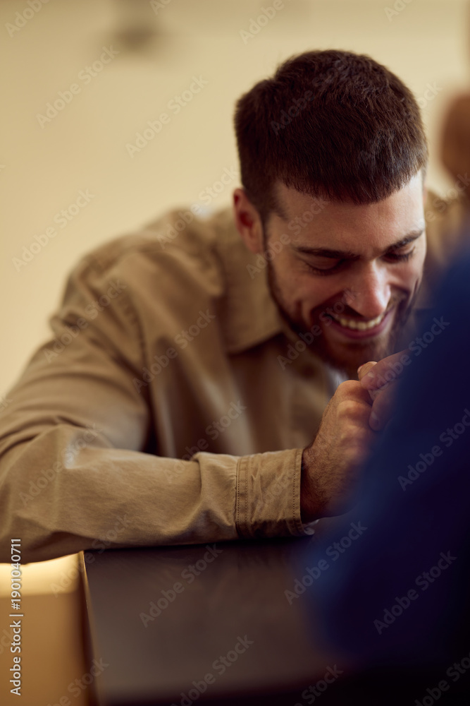 Obraz premium Smiling Man At Diner Table Leaning Forward With Hands clasped, Casual Friendly Moment