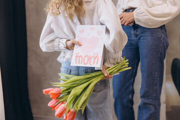 Daughter surprising her mother with tulips and handmade greeting card for Mother's Day