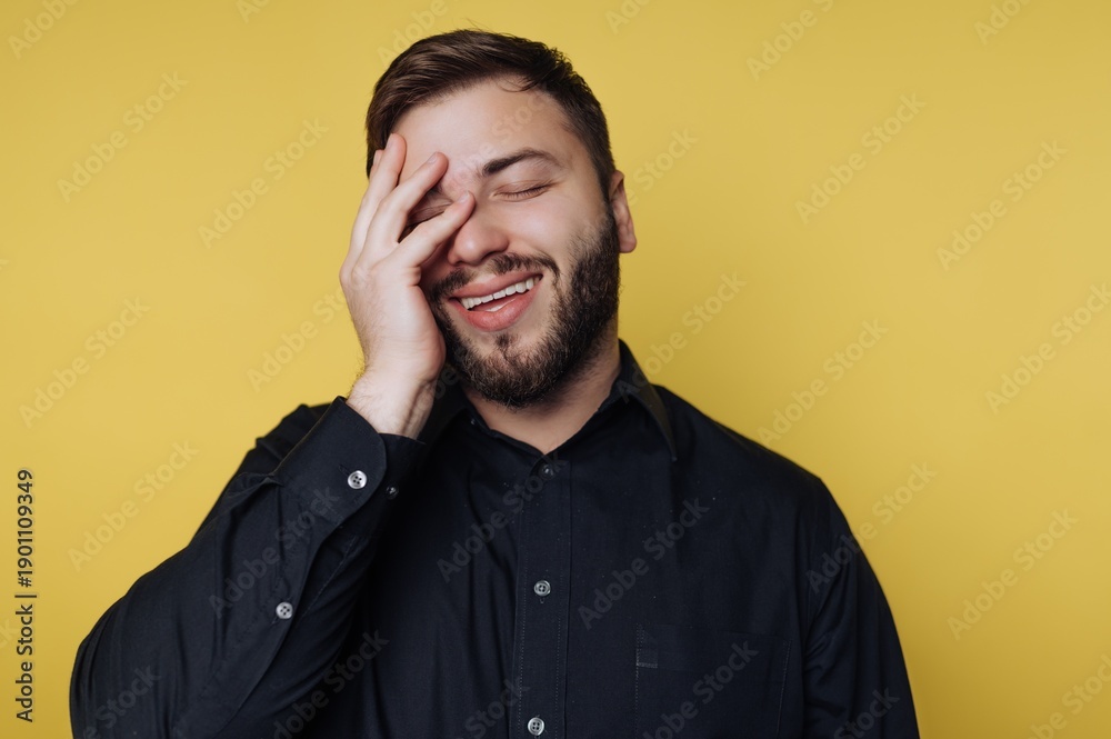 Obraz premium Man smiles and covers his face with hand against a yellow background while expressing a moment of joy