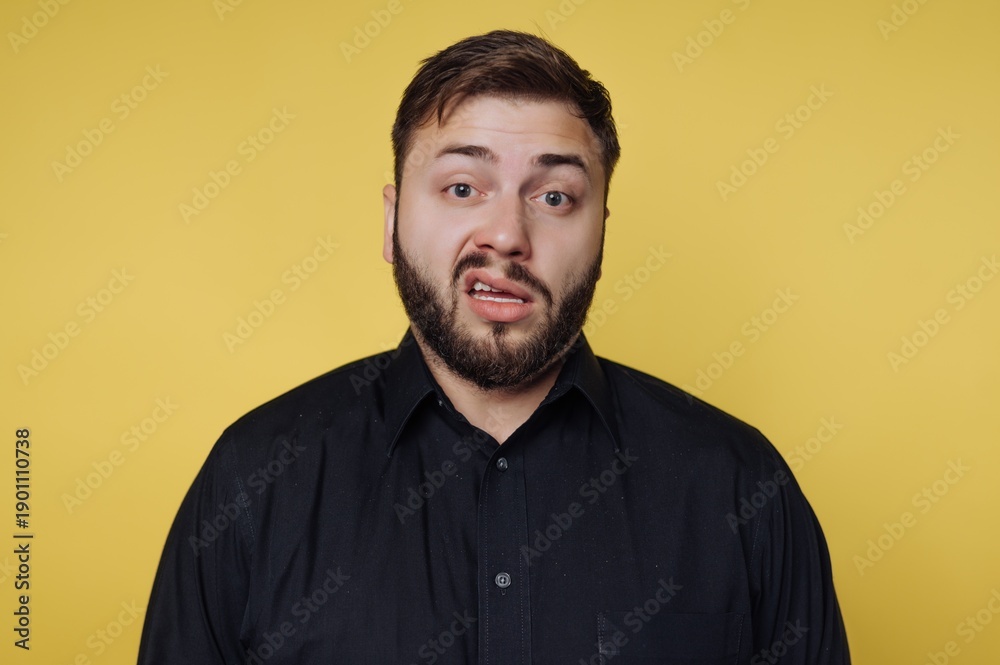 Obraz premium Man makes a funny face on a yellow background while wearing a black shirt and looking at the camera