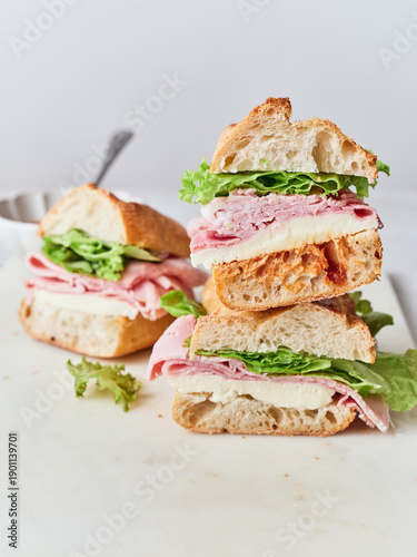 Fresh sandwiches made with baguette, mozzarella cheese, ham, lettuce, and tomato sauce on a lunch table