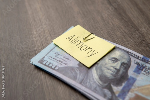 US dollar banknote clipped with a yellow note labeled alimony. Divorce payments, financial obligation, spousal support concept.