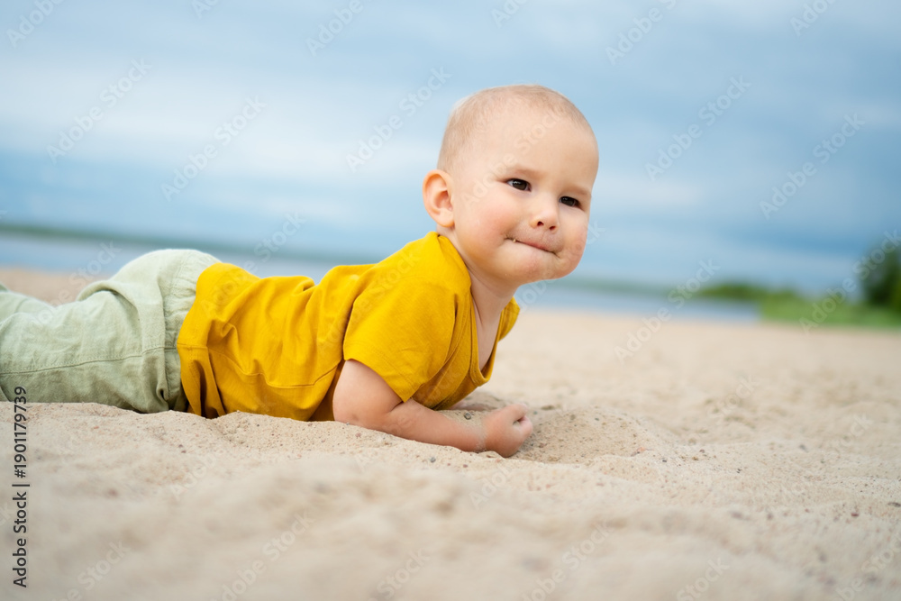 Fototapeta premium A happy toddler in a yellow shirt discovers the texture of sand on a bright beach day, embodying the wonder and excitement of exploring nature playground.