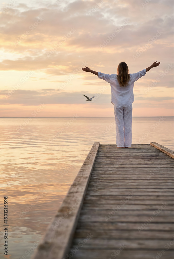 Fototapeta premium A woman finds peace and liberty as she stands on a wooden pier, embracing the freedom of the calm ocean.