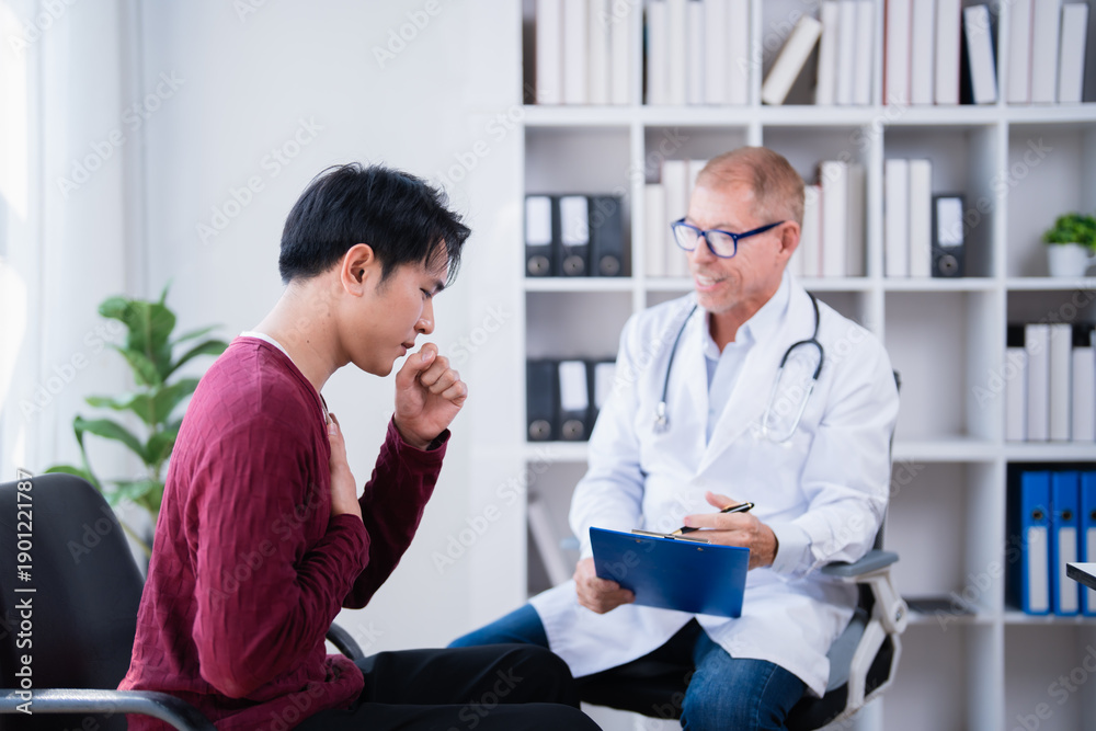 Obraz premium Patient explains symptoms to a doctor during a consultation, covering his mouth while coughing, with the doctor observing and holding a clipboard, discussing health issues in a clinic