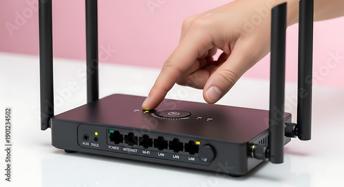 Hand Pressing Button on Black Wireless Router on White Table