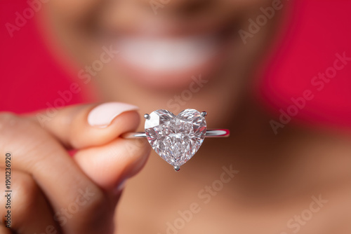 Closeup view of a black woman's hand holding a heart shaped valentine's day diamond ring, copy space of blurred face