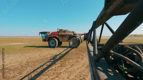 A cinematic shot of agricultural work featuring a self-propelled sprayer moving across an open field, showcasing the scale and precision of modern farm machinery. 