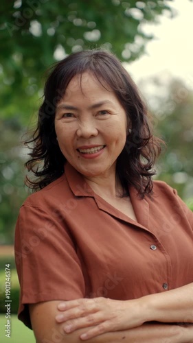 Vertical portrait of smiling senior asian woman 60 years old with urban natural park background, happy retirement lady with healthy aging in life security protection insurance for future planning. 
