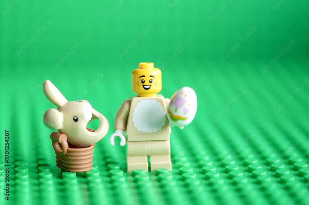 Fototapeta premium Lego minifigure Easter bunny and easter egg on green background with copy space