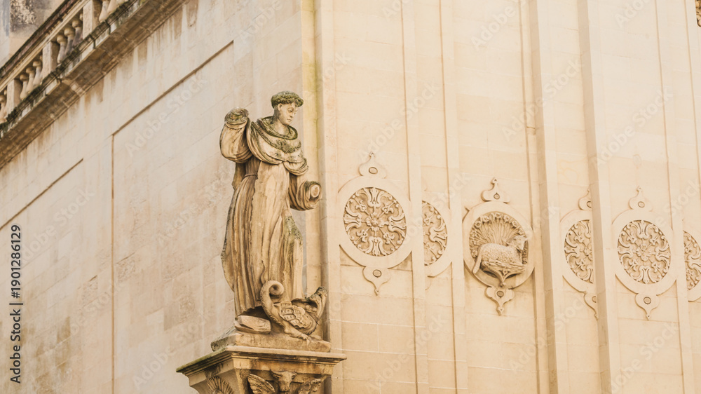 Fototapeta premium Old town in Italy, damaged sculpture of a saint without hands on the church, characteristic sandstone buildings in Lecce