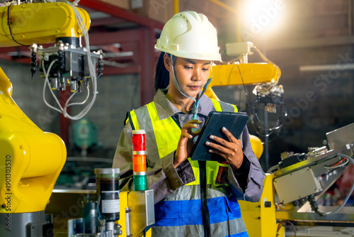 The engineer examines data on a tablet near the robot arm regarding industrial automated manufacturing processes technological safety devices and factory workflows.
