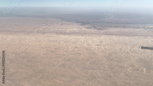 Aerial view of an endless desert landscape seen from above. Natural arid terrain with sand patterns and atmospheric haze. Travel, nature and environment concept.