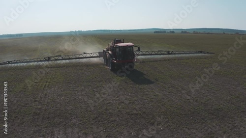 Aerial footage of agricultural operations showing a self-propelled sprayer with a wide boom moving evenly across an open field to ensure precise and efficient crop treatment. 