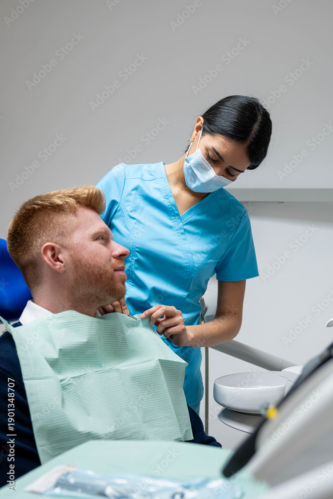 Fototapeta premium Dental assistant placing a bib on a smiling male patient in a dental clinic