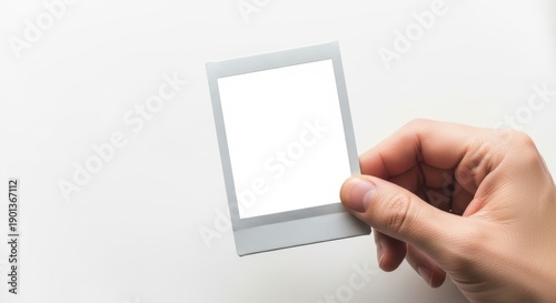 Hand holding an empty instant photograph with a white background, perfect for custom content creation or nostalgic memories