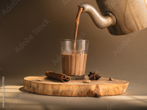 Indian chai served in glass cups, brewed in a metal kettle with aromatic masalas, getting poured on cup.