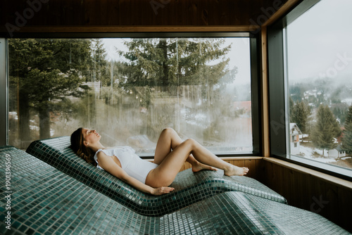 Tablou pe pânză Relaxing woman enjoys peaceful spa experience on warm stone bed with scenic moun