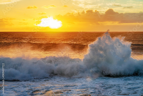 Foto Dramatic ocean waves crashing under warm golden sunset light with glowing clouds and dynamic sea spray
