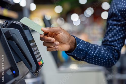 Obraz na płótnie Person's hand holding a credit card near a pos terminal, performing a secure and