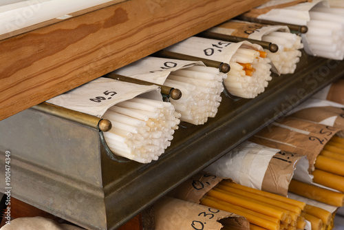 A close-up view of neatly stacked beeswax and white candles on wooden shelves in an Orthodox church shop, reflecting faith, religion, and spiritual tradition.
