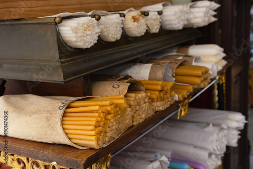 A close-up view of neatly stacked beeswax and white candles on wooden shelves in an Orthodox church shop, reflecting faith, religion, and spiritual tradition.