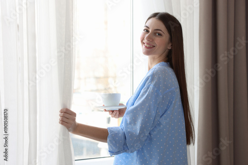 Woman with cup of drink opening window curtains at home Free Download Woman with cup of drink opening window curtains at home - GFXLoad